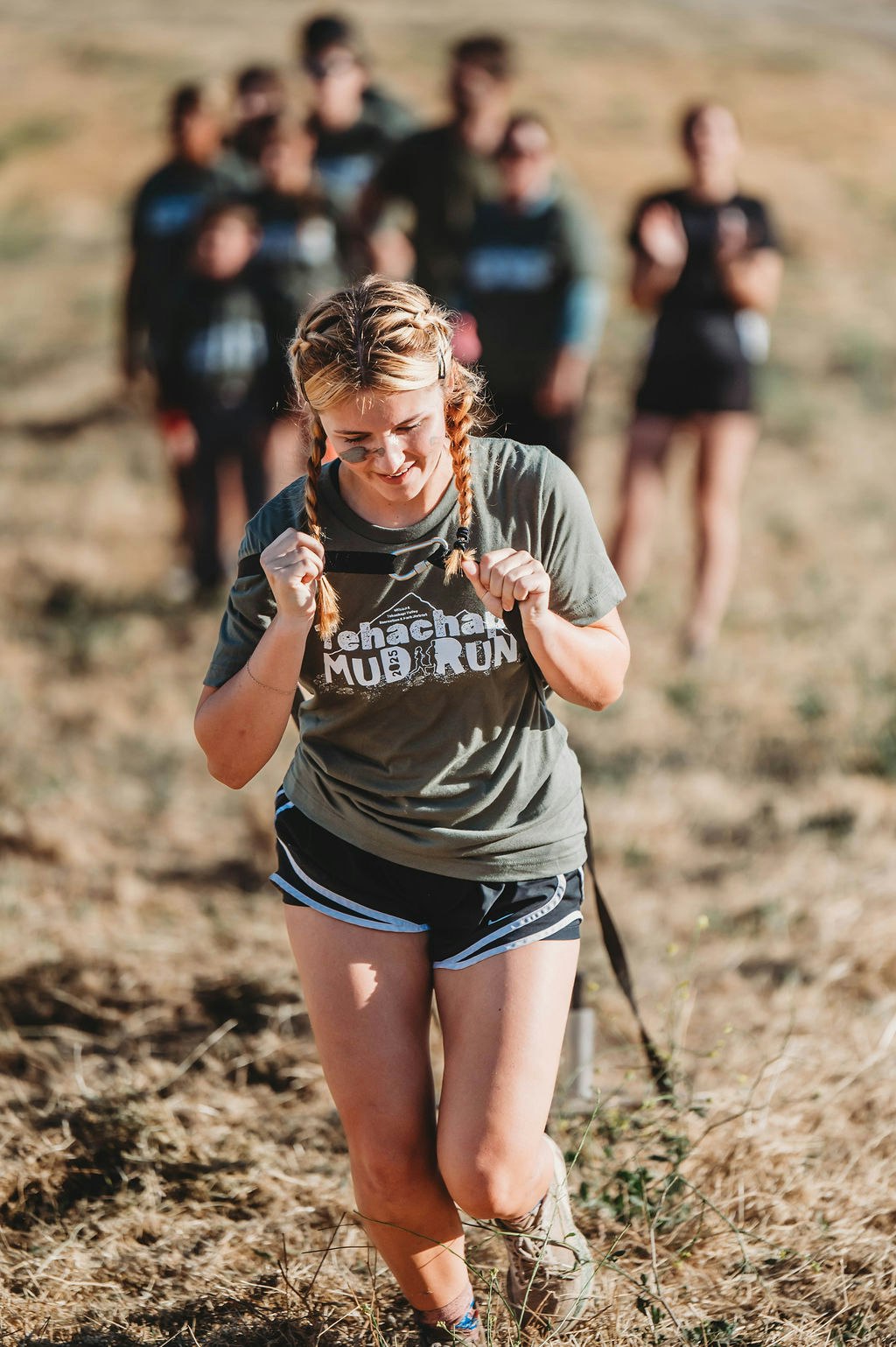 Person running uphill with a group in the background, wearing a "Mud Run" t-shirt.