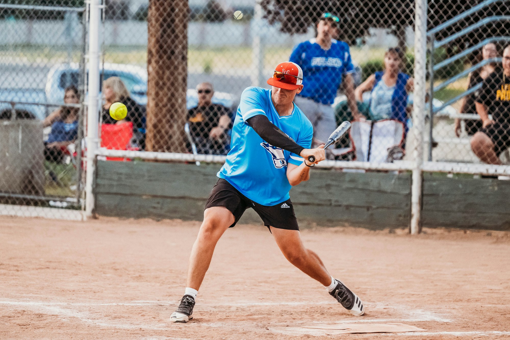 A player swinging at a pitch in a softball game with spectators in the background.