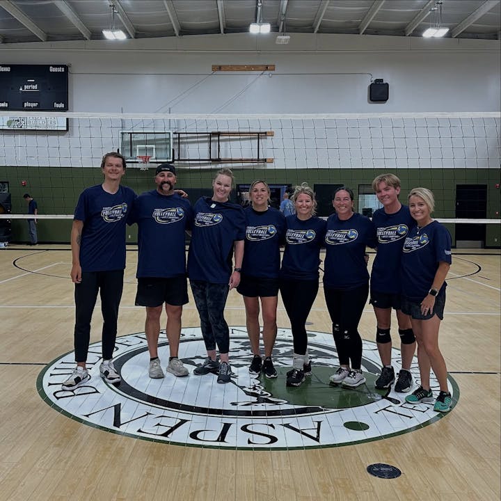A group of people in matching volleyball shirts standing on a court in a gym.