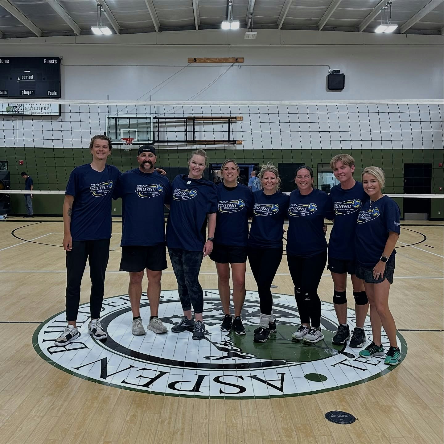 A group of people in matching volleyball shirts standing on a court in a gym.