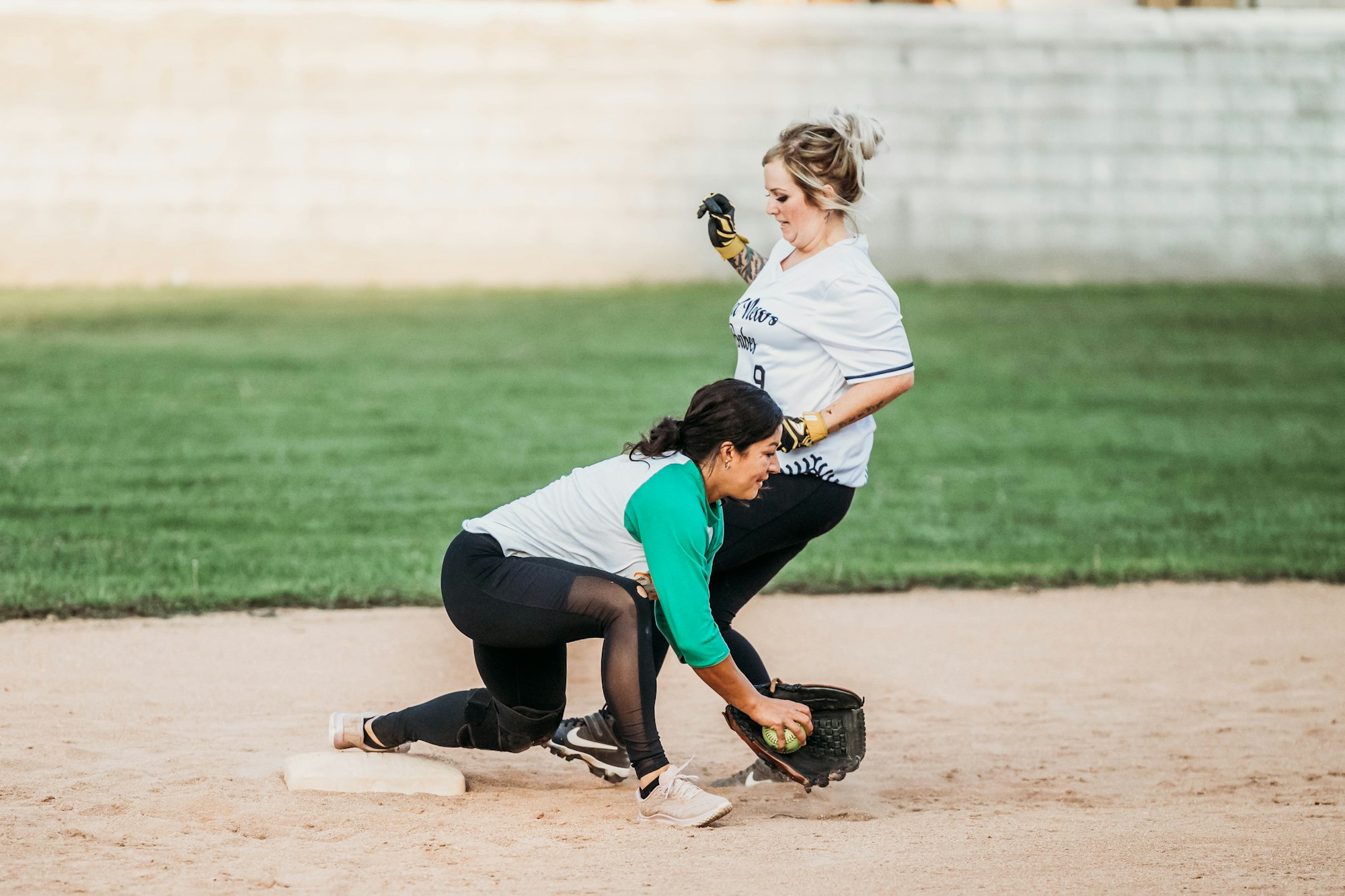 Two women playing softball, one sliding into base while another attempts to tag her out.