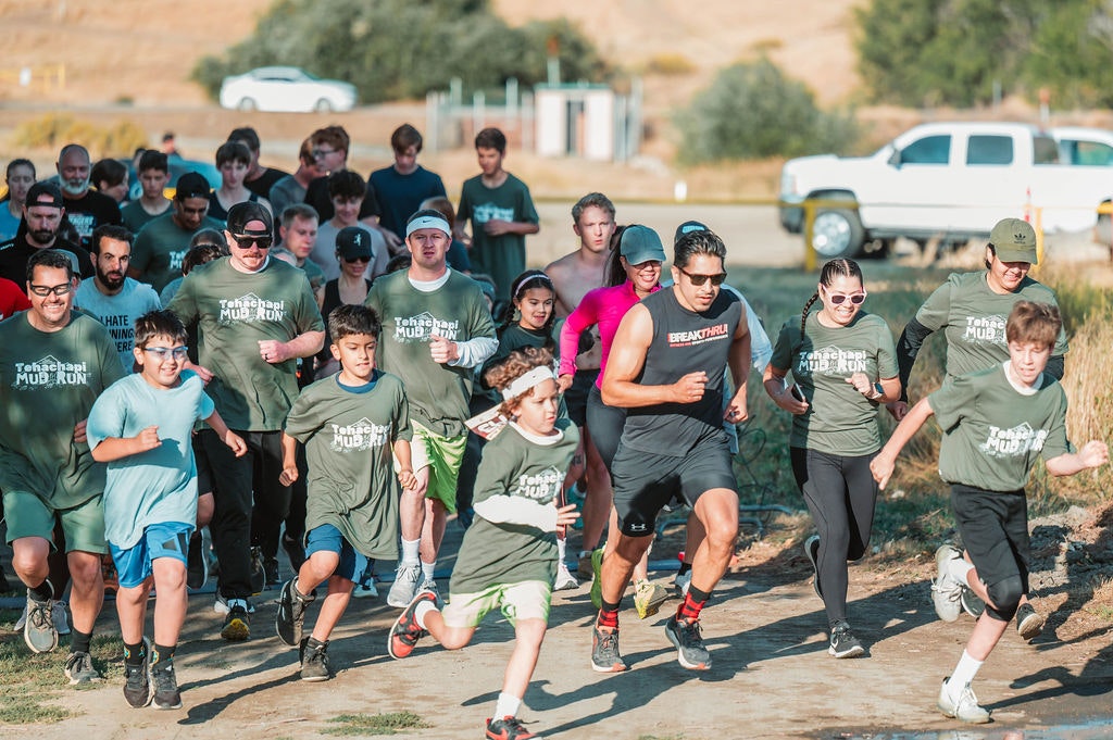 A group of people participating in a mud run outdoors, wearing themed shirts, running energetically together.