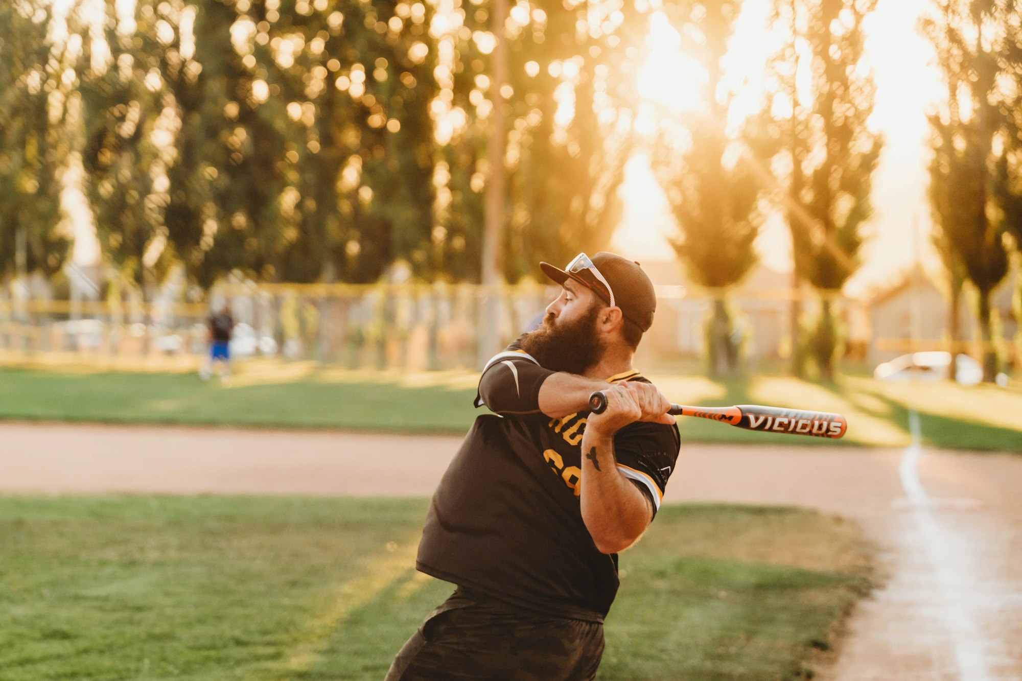 A man swinging a baseball bat at sunset on a field.