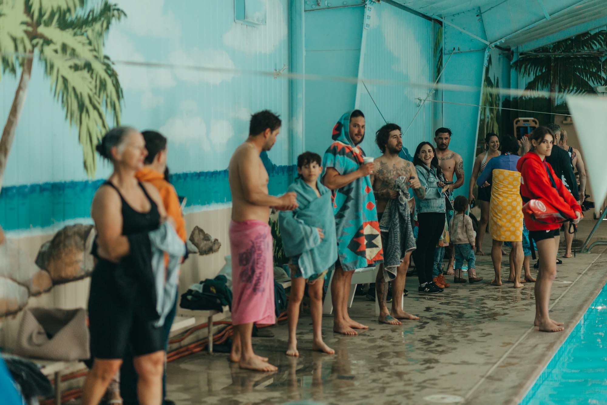 A group of people wrapped in towels by an indoor pool.