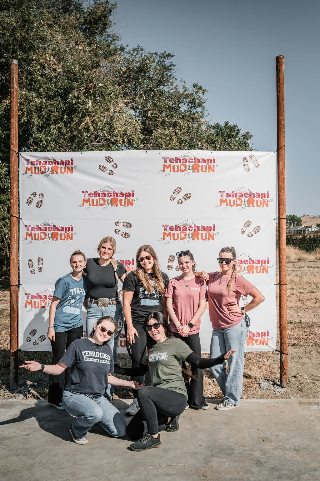 A group of people posing in front of a "Tehachapi Mud Run" banner outdoors.