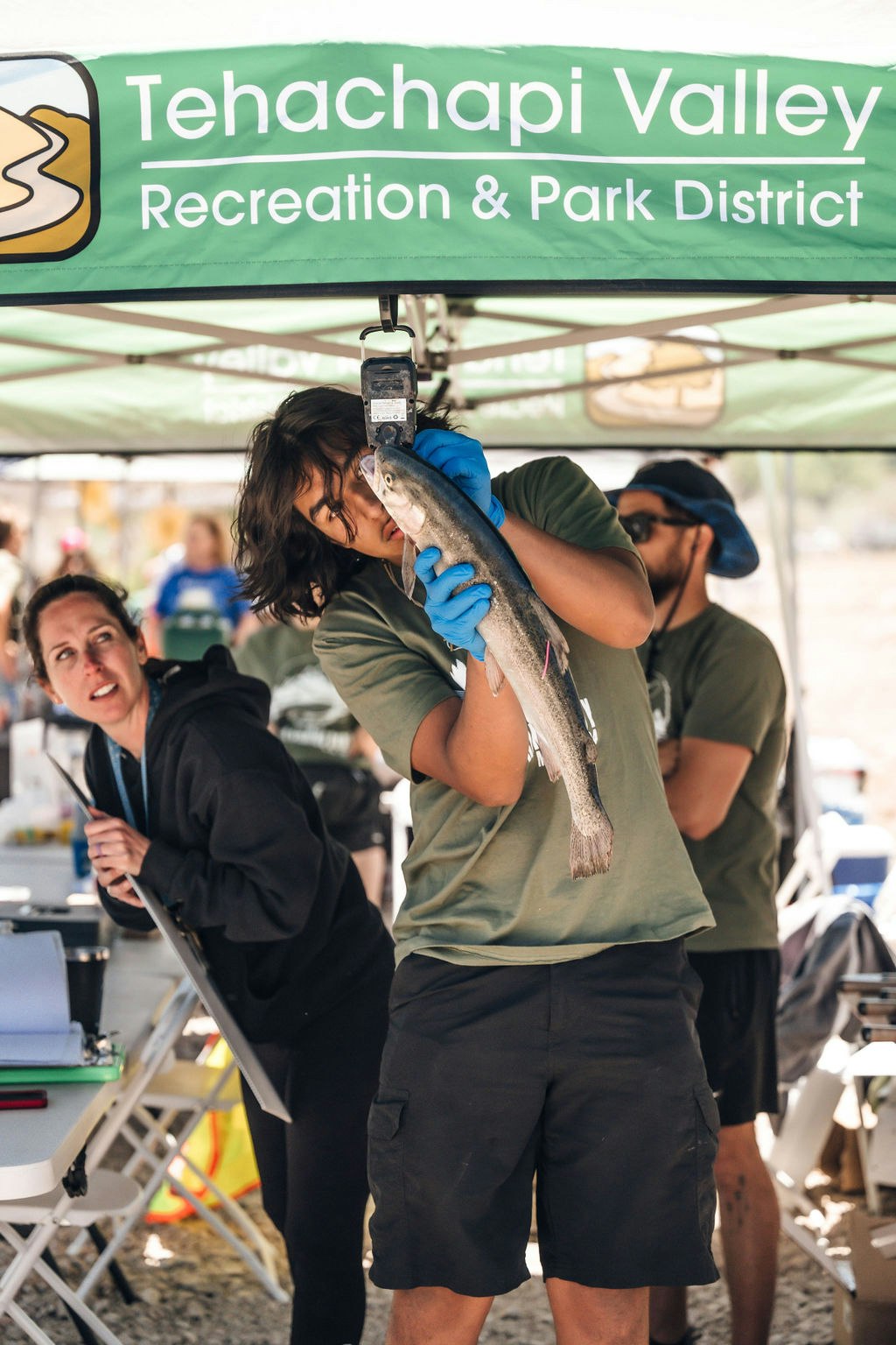 Person weighing fish at an event under "Tehachapi Valley Recreation & Park District" banner.