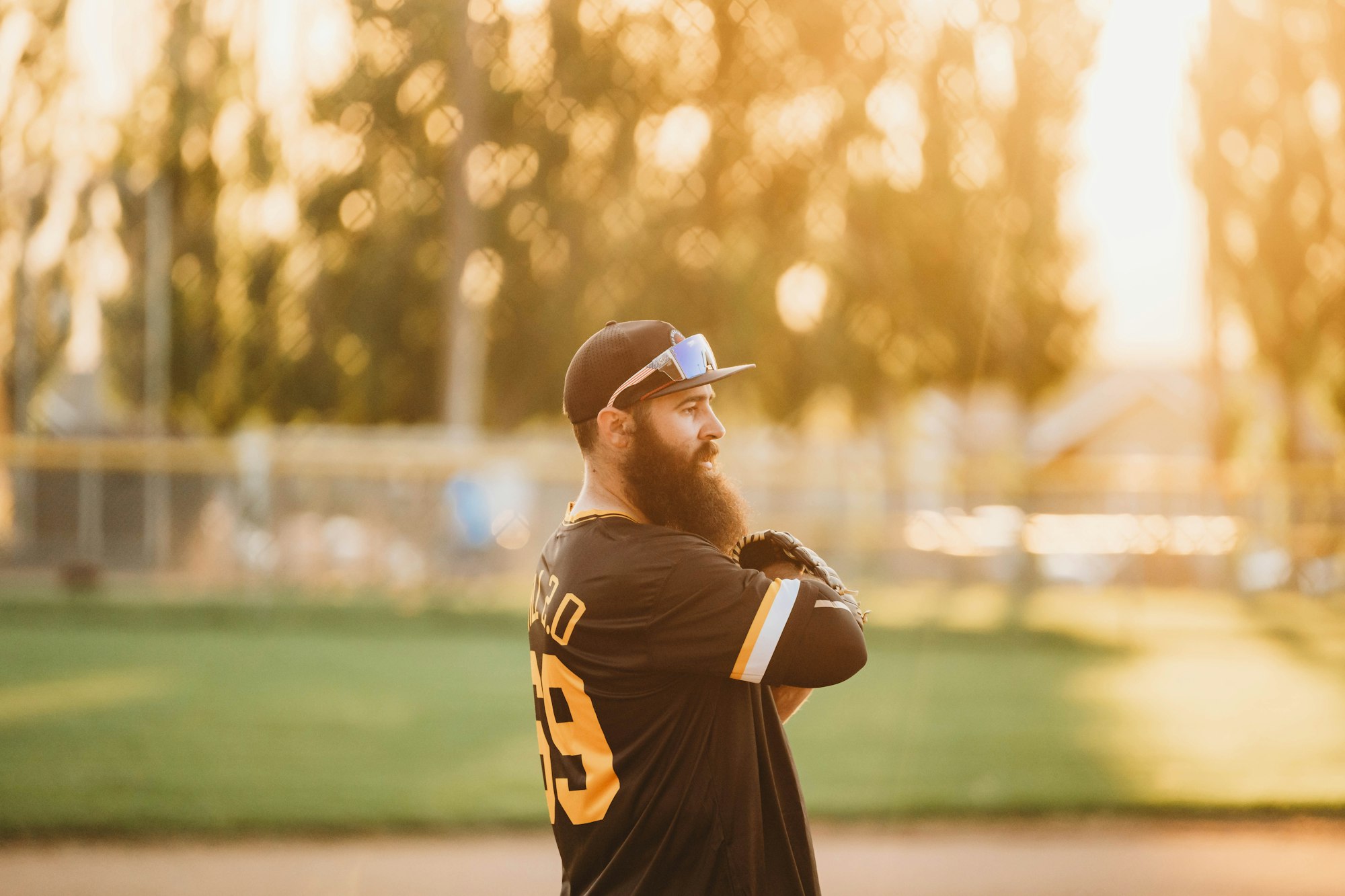 A bearded man in a baseball uniform stands on a field at sunset, looking thoughtful.