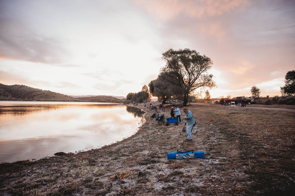 People by a lake at sunset, with a serene landscape and reflections on the water.
