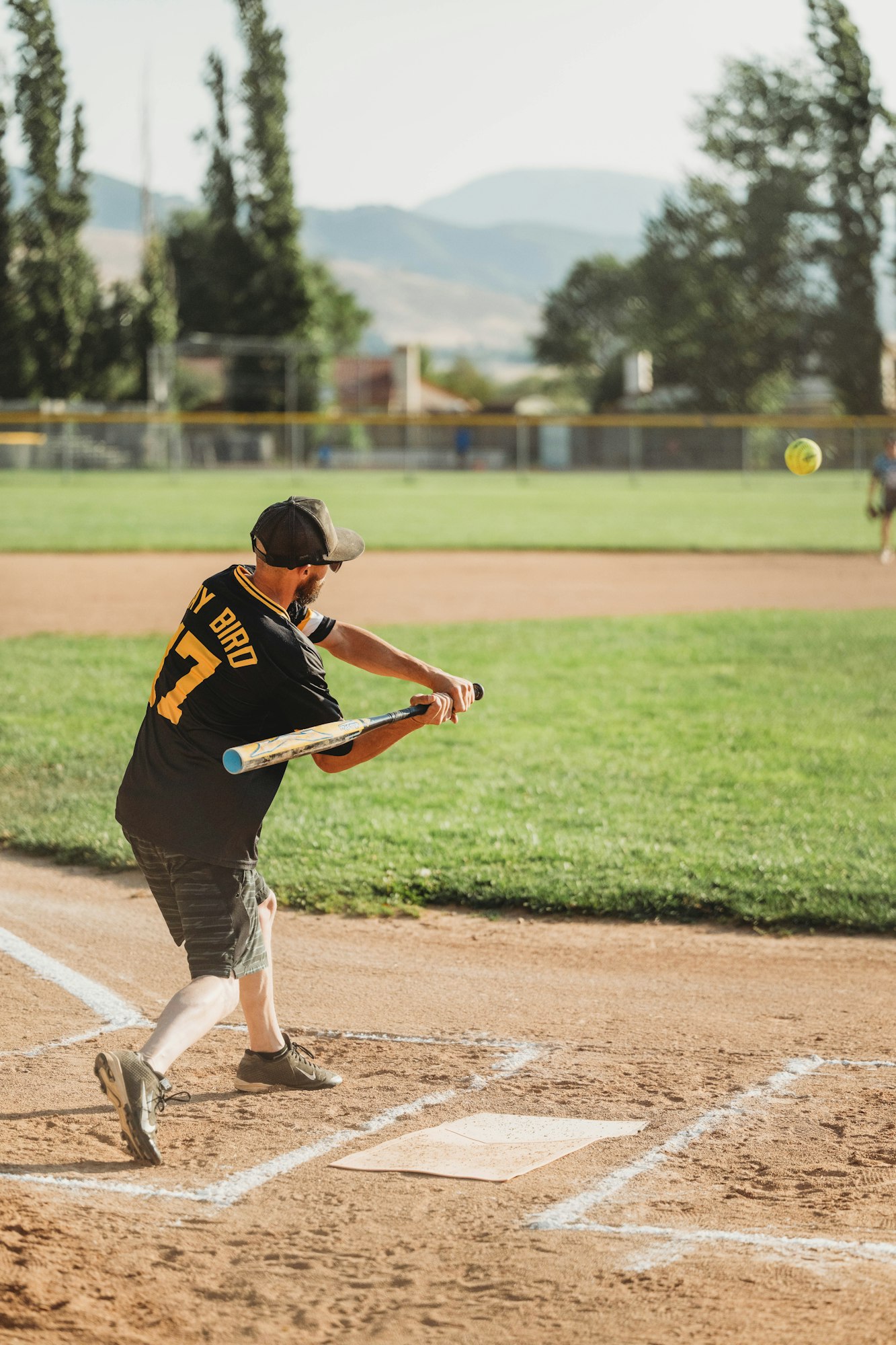A person swinging a bat at a softball on a sunny field.
