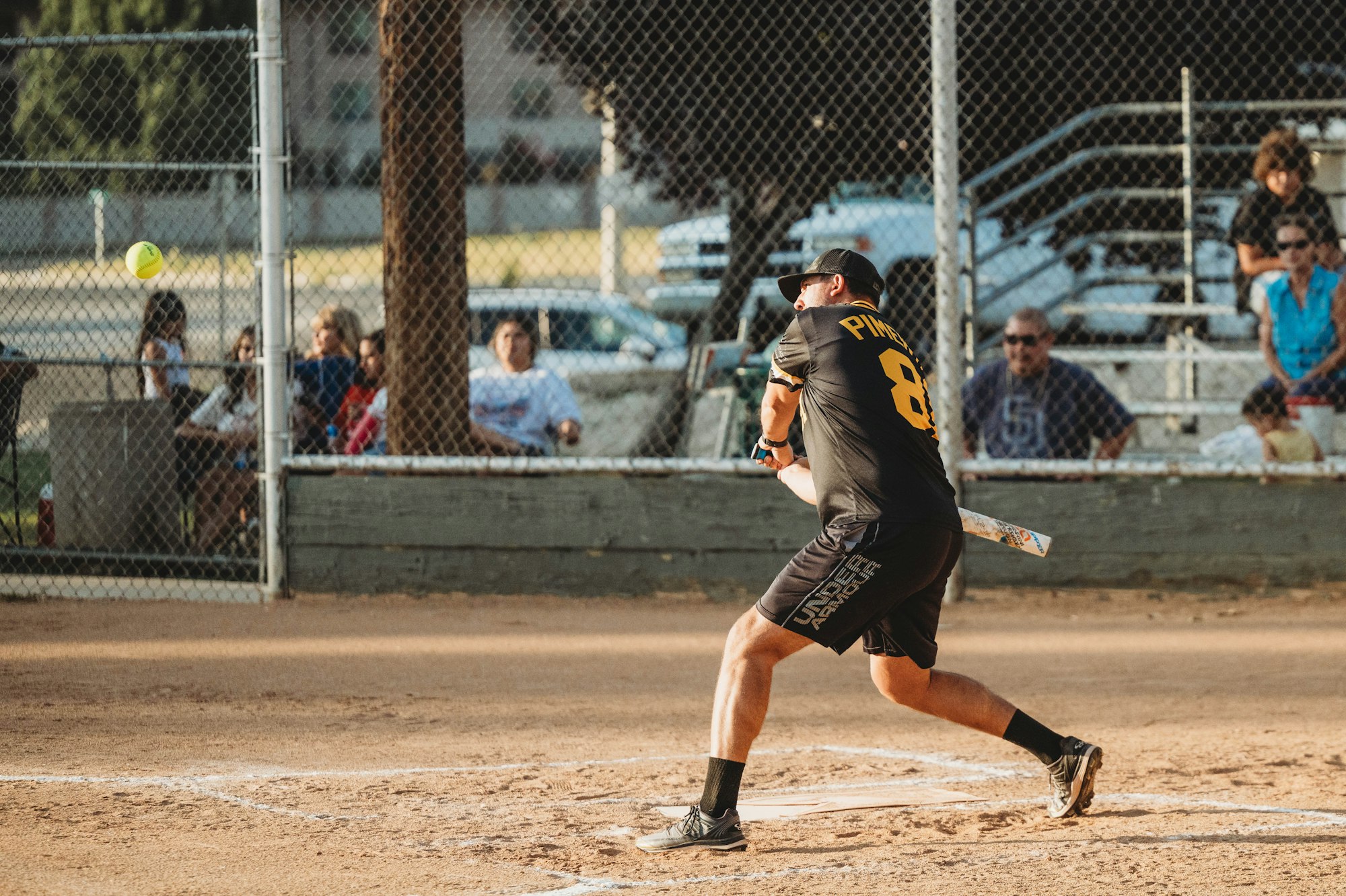 A player swinging at a pitch in a softball game with spectators in the background.