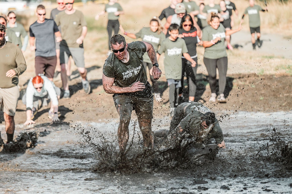 People running through a muddy obstacle course, splashing water and dirt.