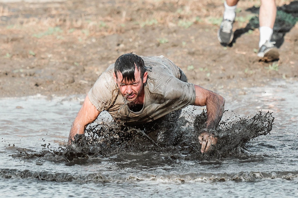 A person crawling through mud during an outdoor obstacle or mud race.