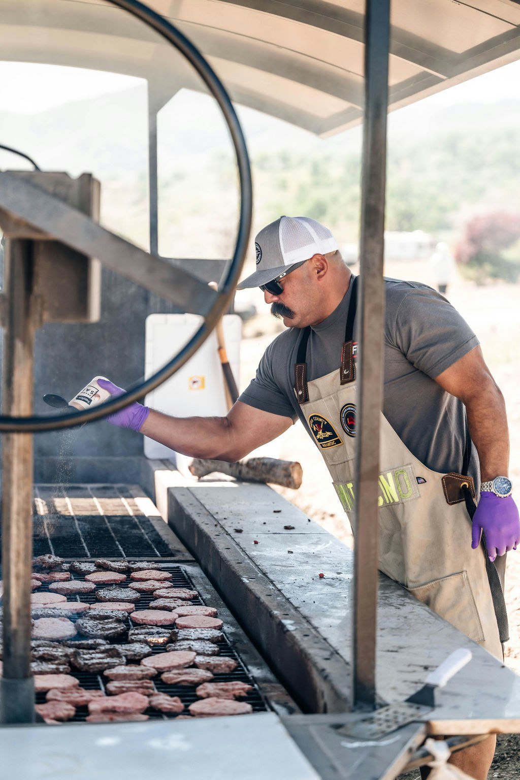 Man in an apron grilling burgers outdoors.