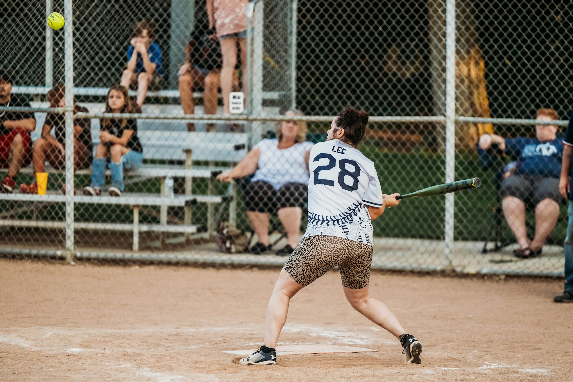 A softball player swinging at a pitch with spectators in the background.