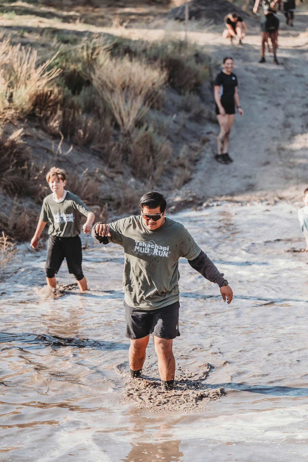 People participating in a mud run, walking through a muddy water course with determination.