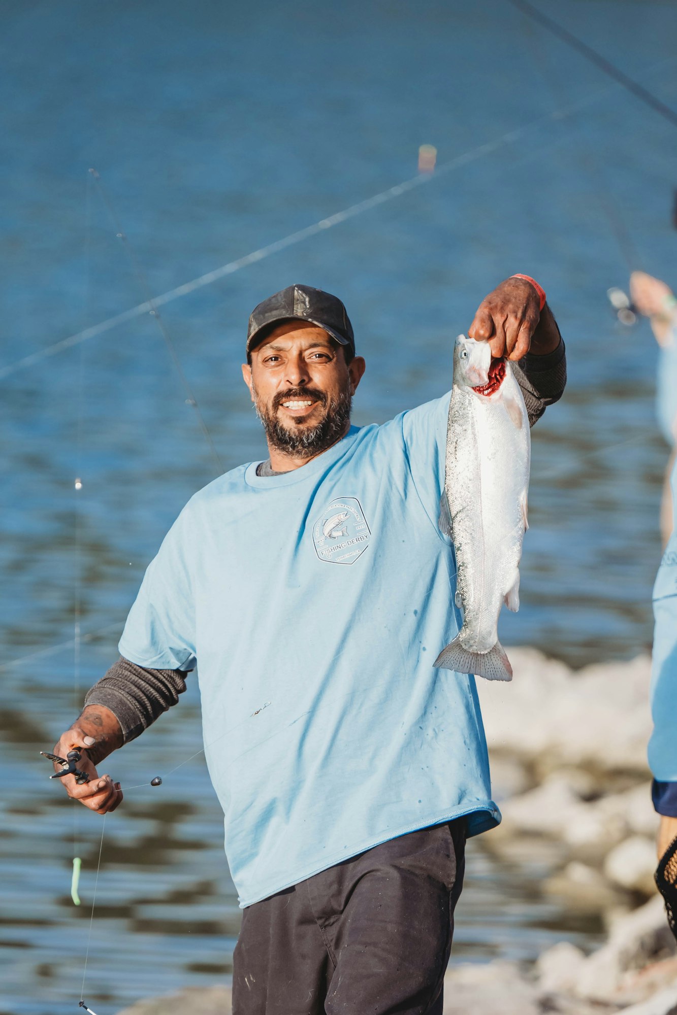A man holding a fish and a fishing rod by the water, smiling.