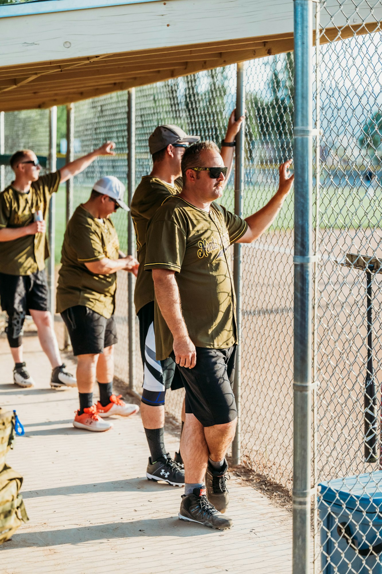 Men in baseball uniforms watching a game from a dugout.
