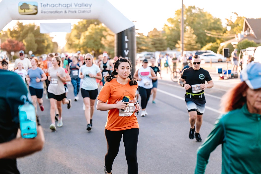 People running a race on a street with a sign reading "Tehachapi Valley Recreation & Park District" in the background.