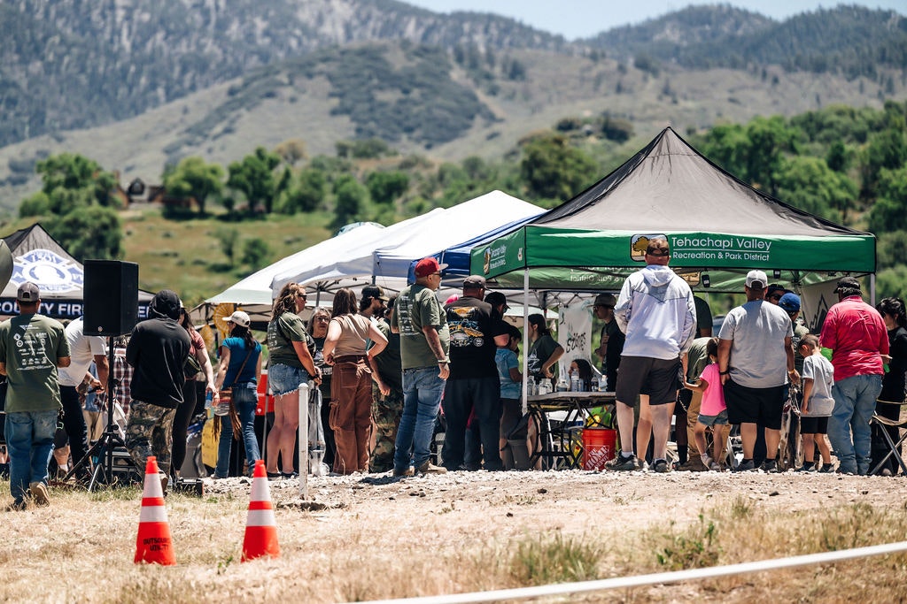 People at outdoor event booths with mountain backdrop.