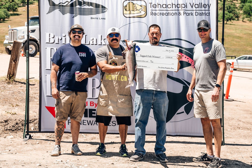 Four men posing with a large check for a "Tagged Fish Winner," indicating a fishing competition prize.