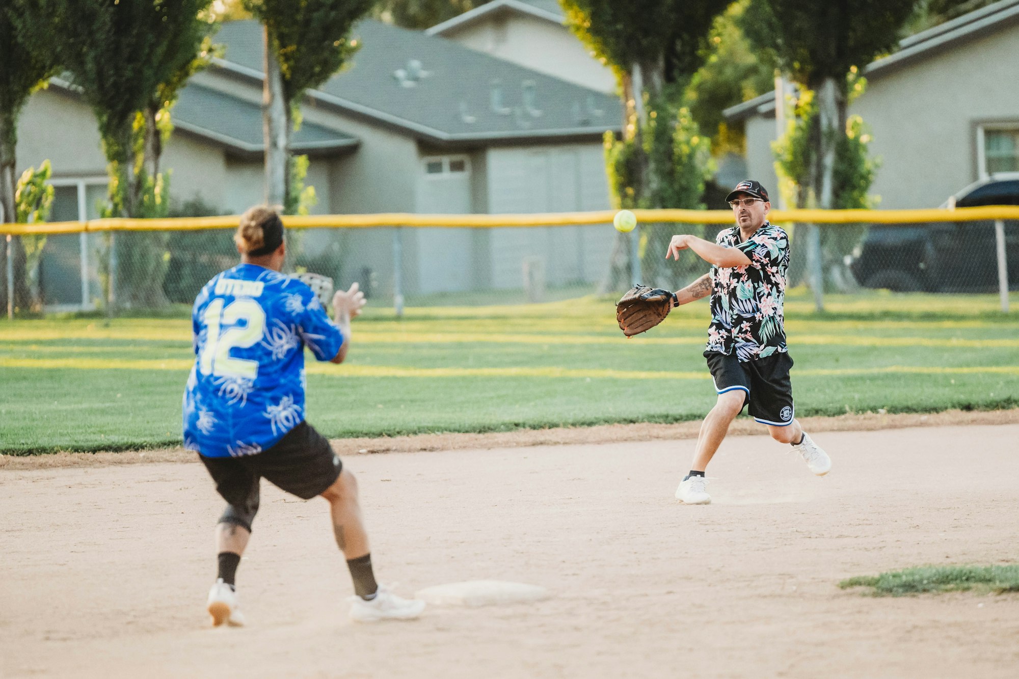 Two players in colorful shirts playing softball, one pitching a yellow ball and the other ready to catch.