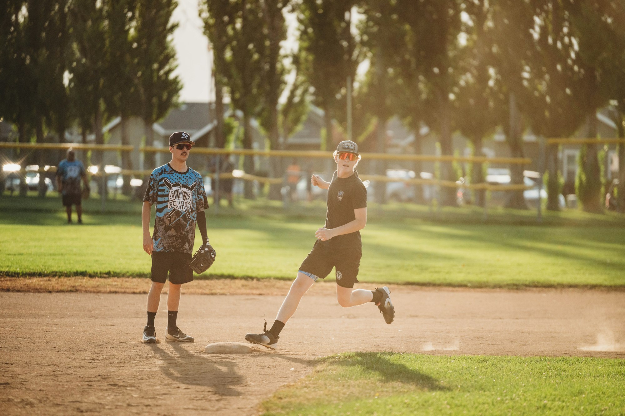 Two people playing baseball on a sunny field, one running bases, the other fielding.
