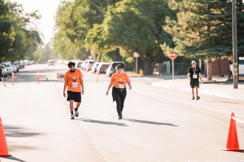 People in orange shirts walking down a street, participating in an event, with traffic cones and trees around.