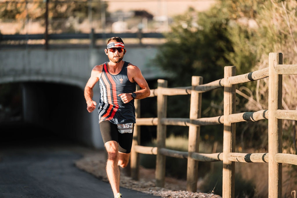 A person running on a path beside a wooden fence, wearing athletic gear, sunglasses, and a visor.