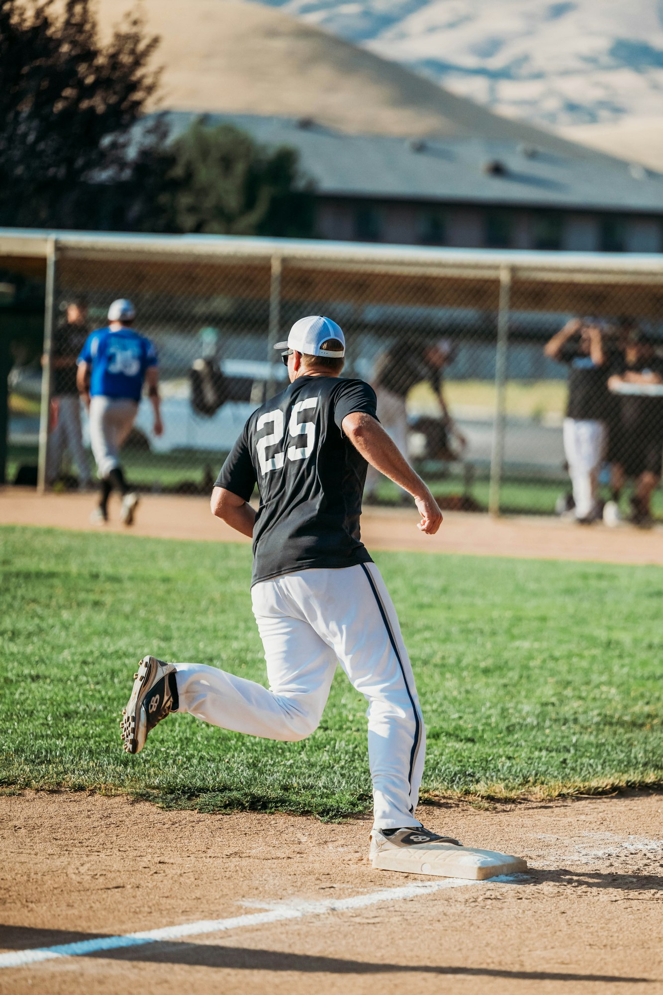 A baseball player (#25) running bases on a field with a scenic backdrop.