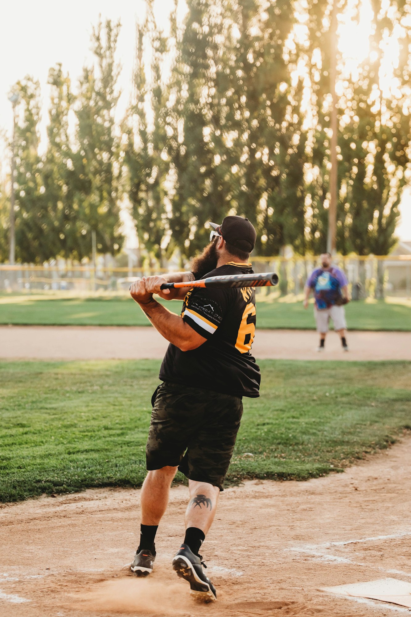 A baseball player swinging a bat at sunset on a dusty field.