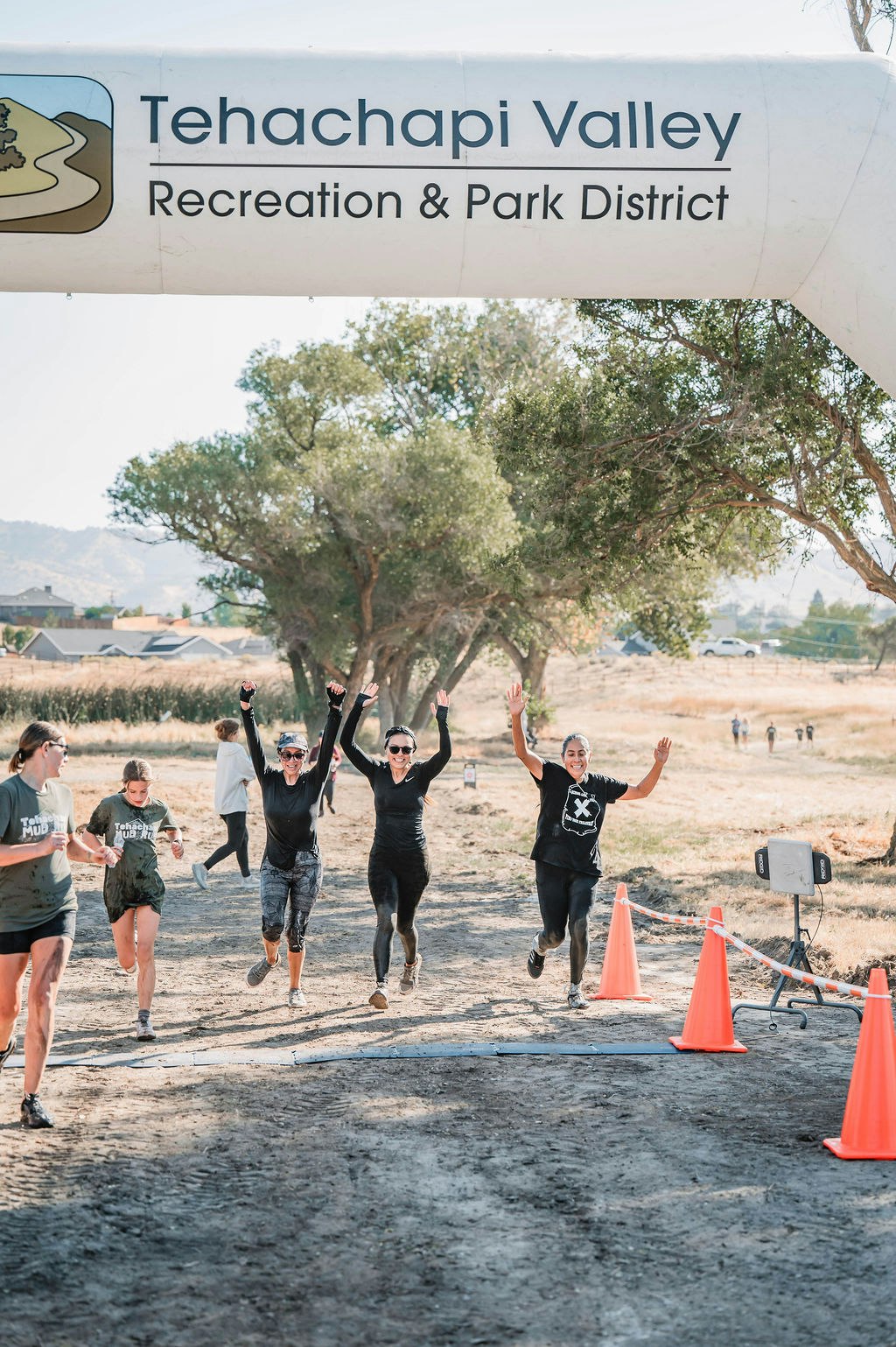 Group of people celebrating as they finish a race under a "Tehachapi Valley Recreation & Park District" banner.