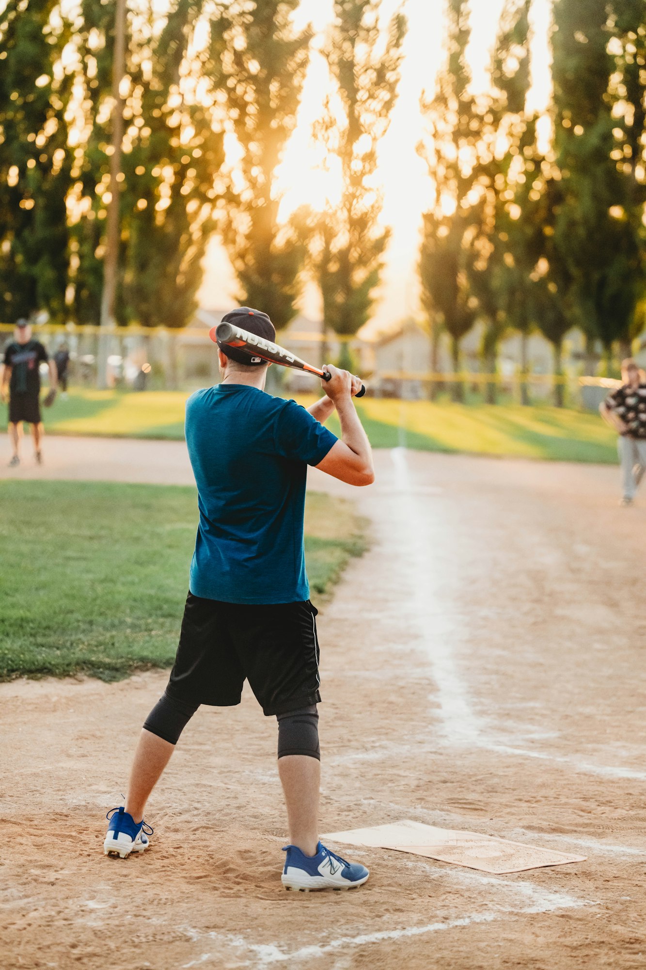 A person is ready to bat at sunset on a baseball field.