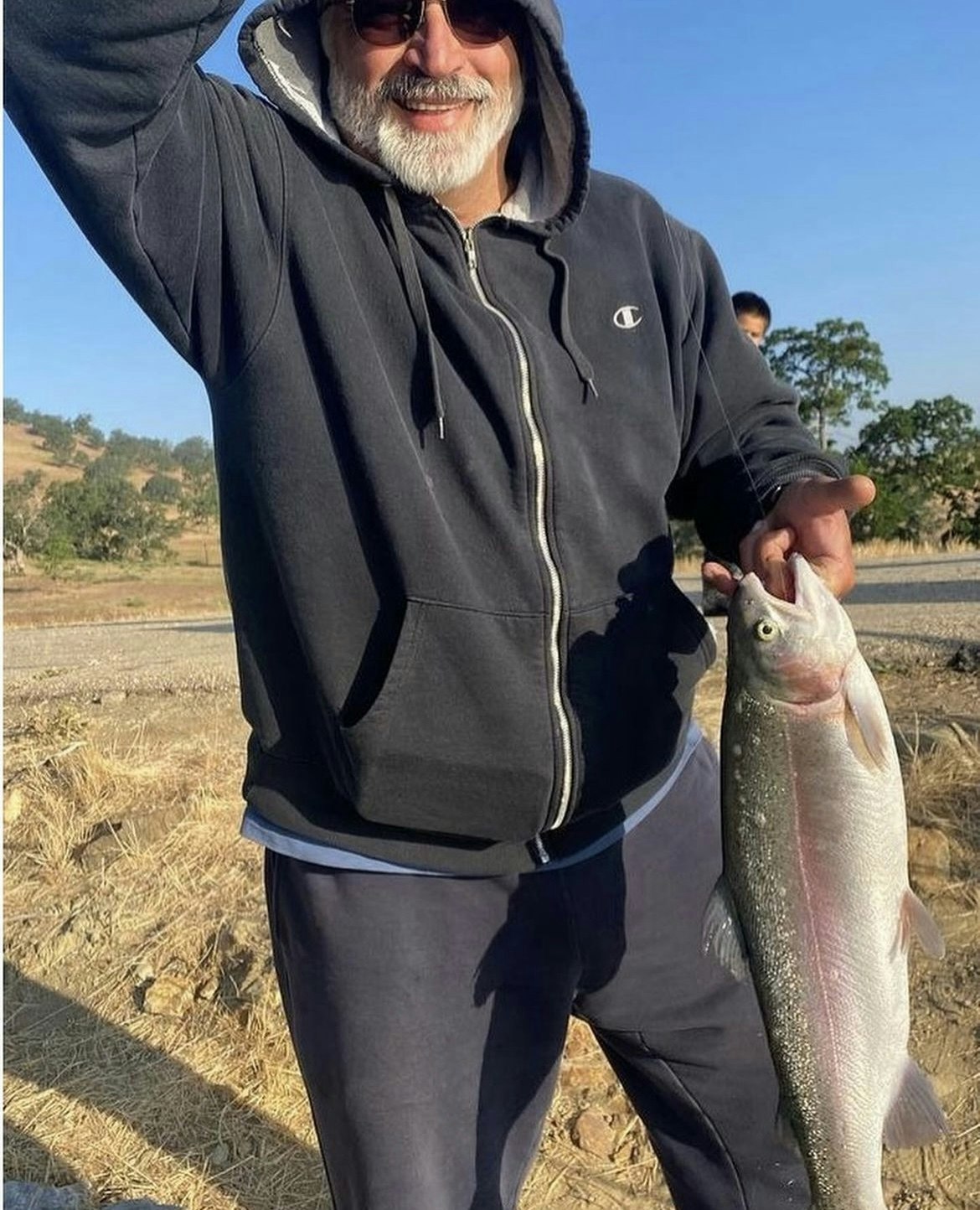 Man holding a fish outdoors with a smile.