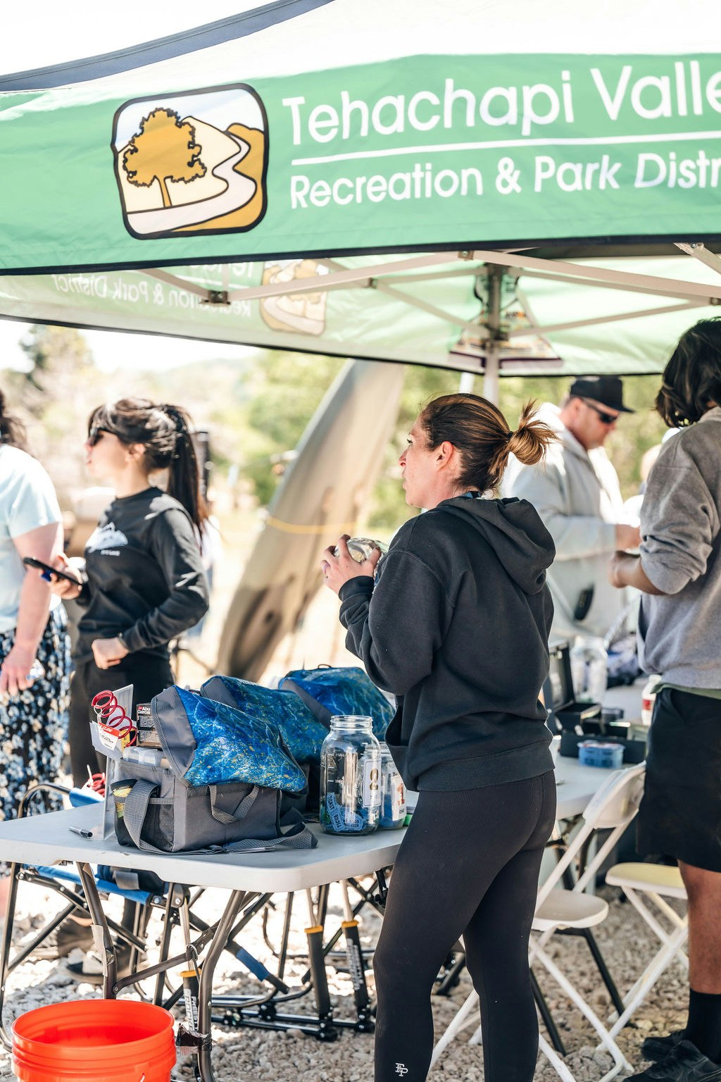 People at an outdoor event with a Tehachapi Valley Recreation & Park District banner. There's a table with supplies and a canopy.