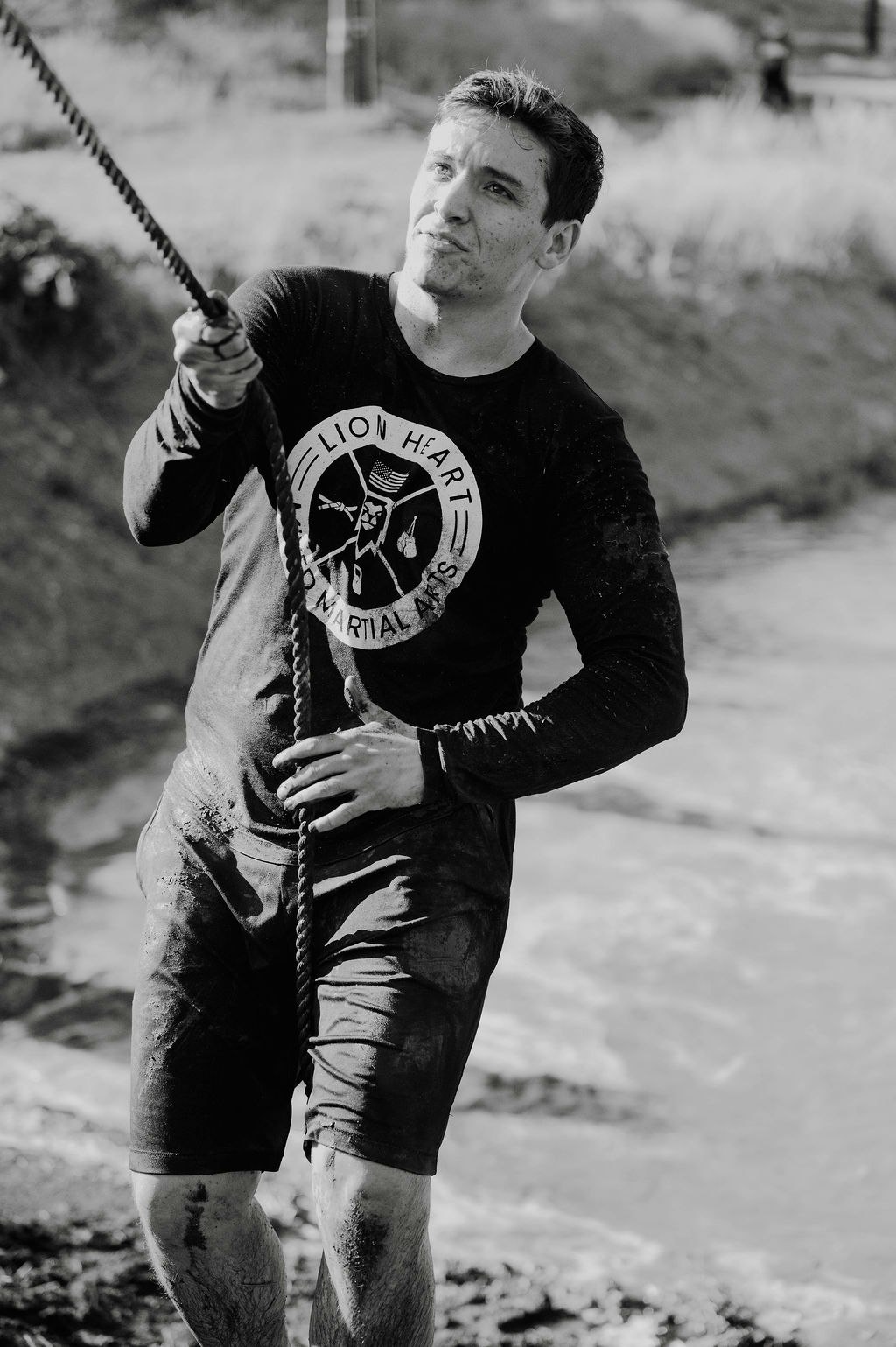 A man in muddy clothes pulls a rope during an outdoor activity.