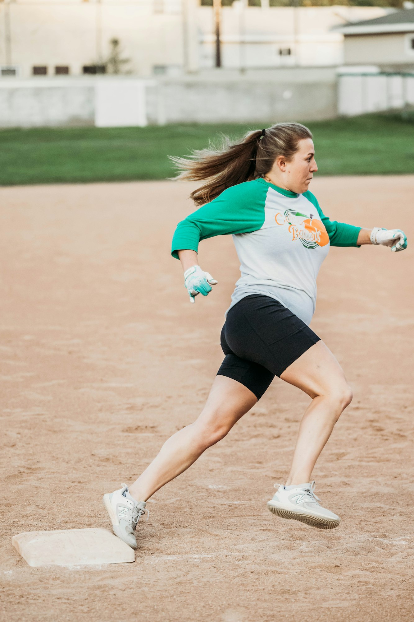 A woman is playing softball, running bases on a dirt field.