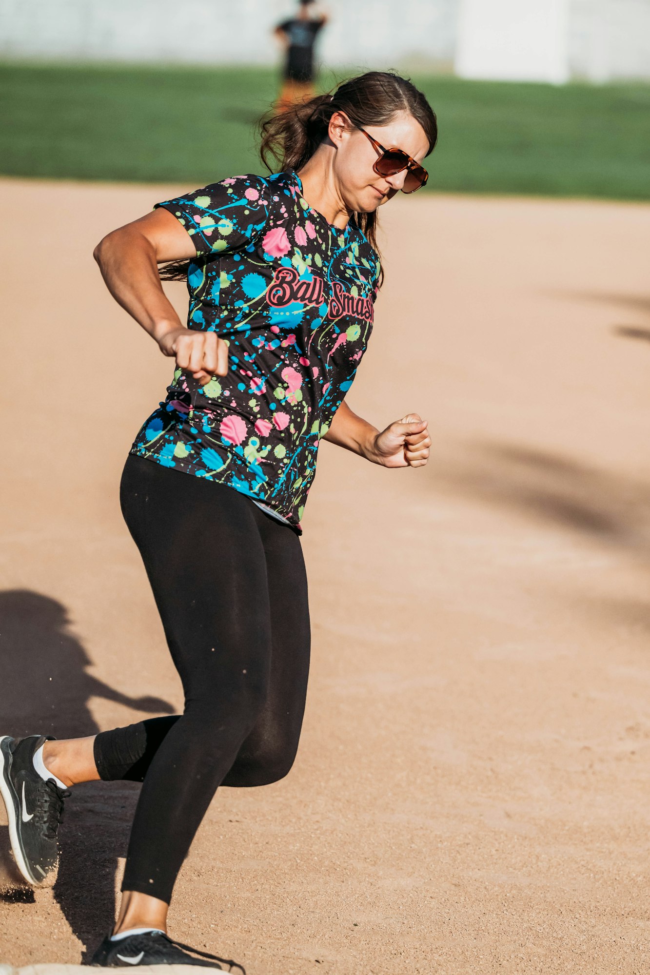 A woman in sportswear and sunglasses is running on a sandy field.