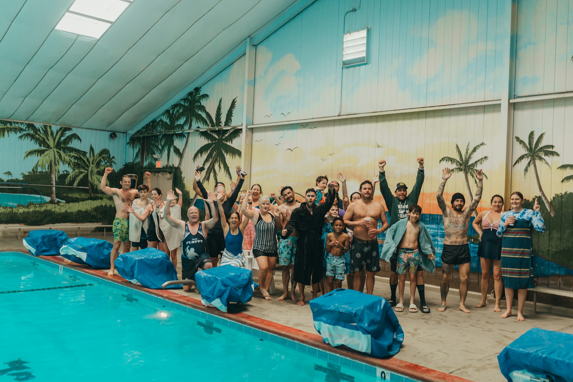 Group of people posing joyfully by an indoor pool.