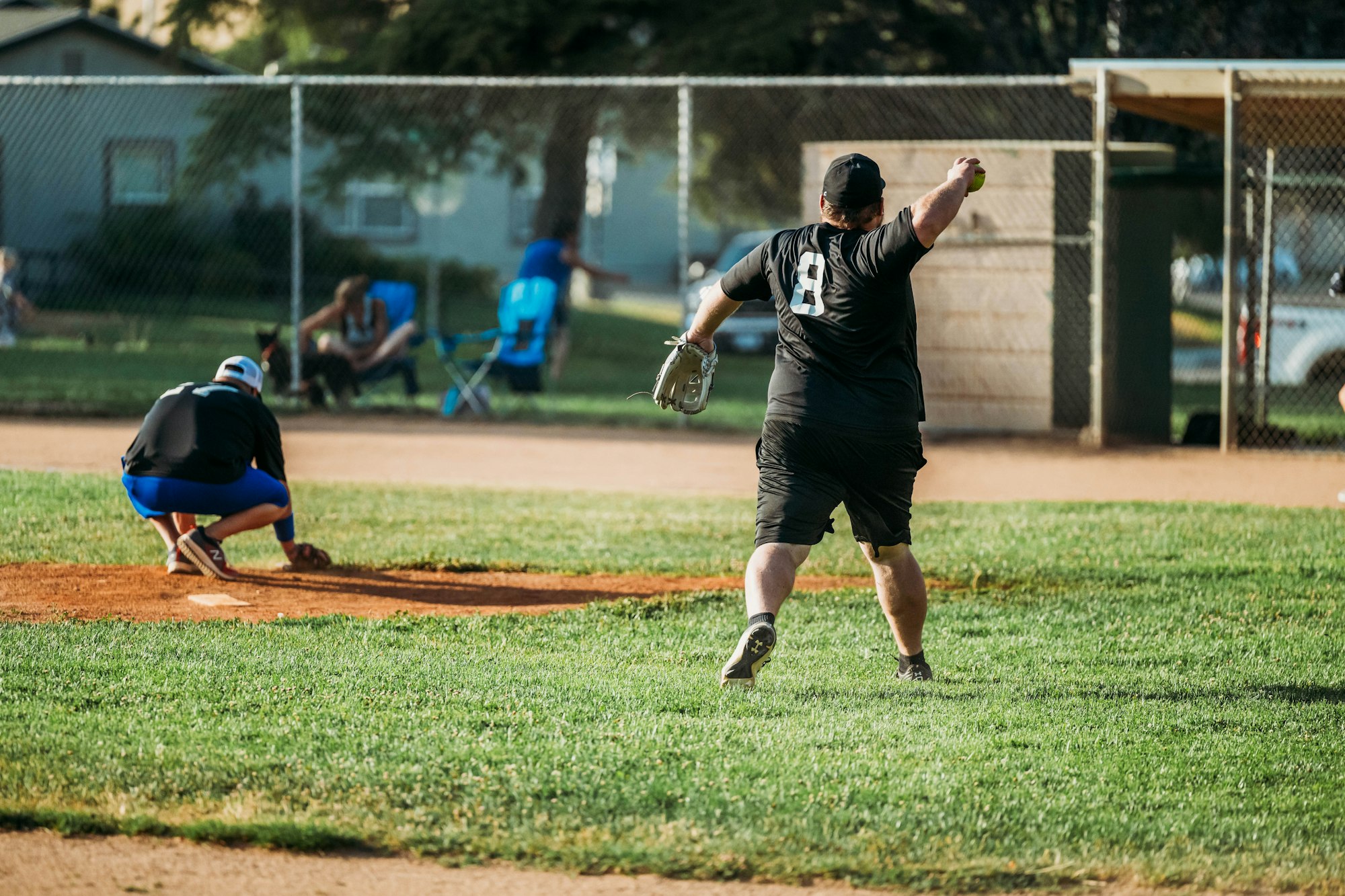 A softball game in progress, with players on the field and spectators in the background.