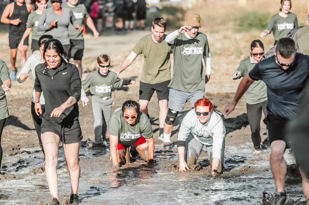 People participating in a mud run, crawling through muddy water and smiling.