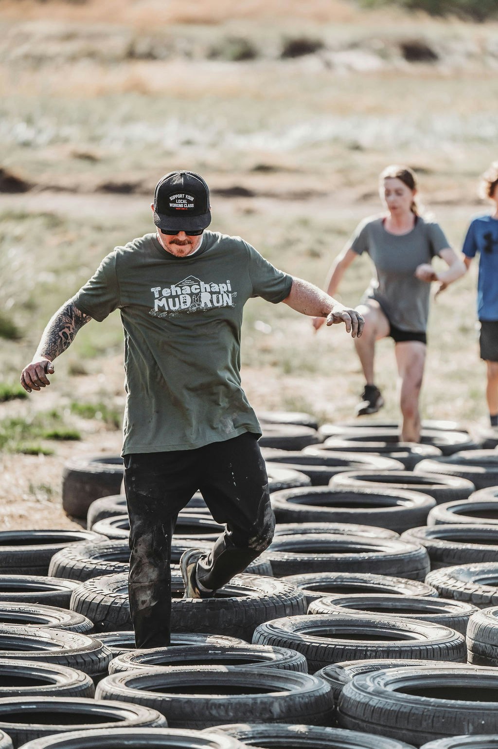 People participating in a mud run, stepping through a series of tires on the ground.