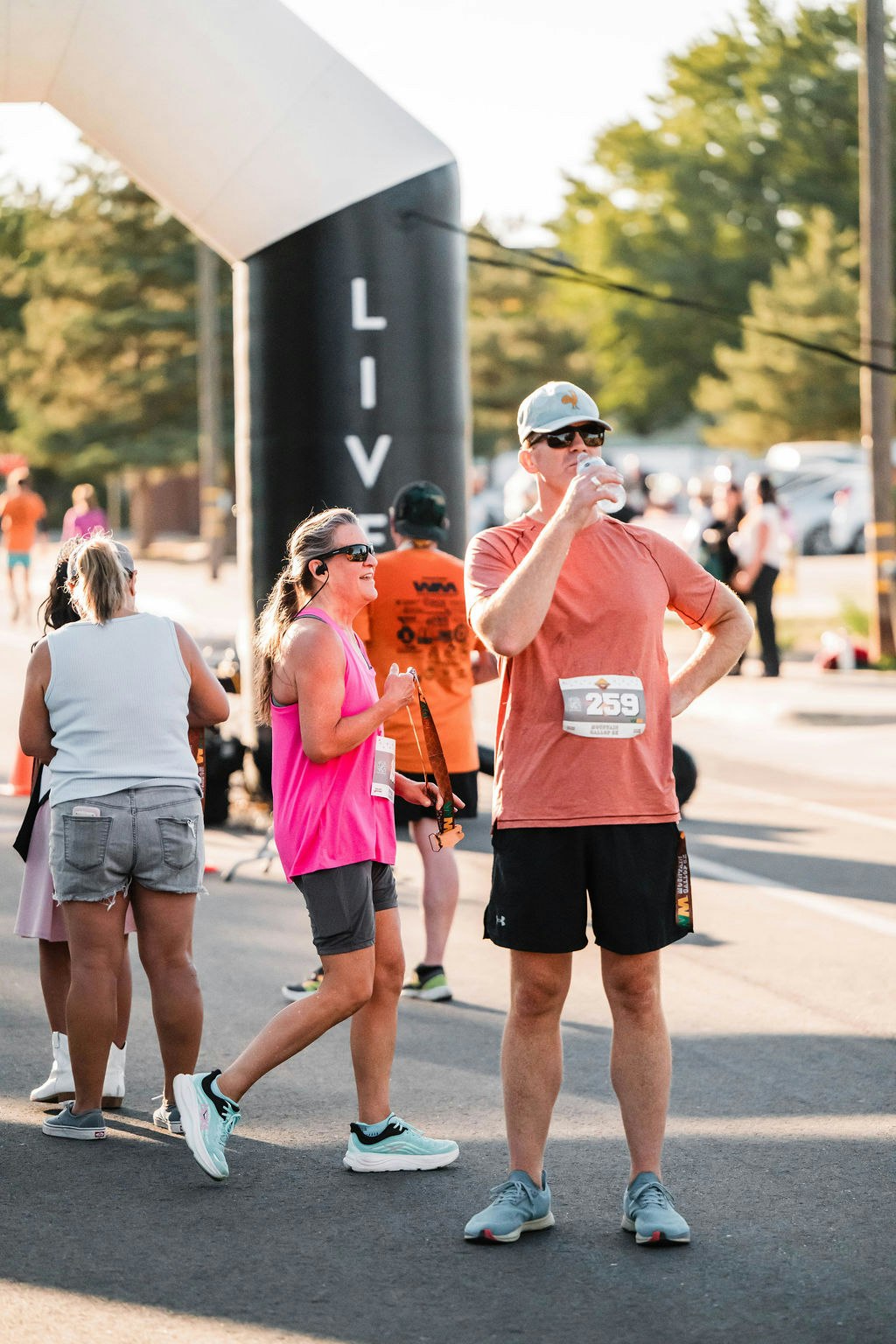 People at a race event; one drinks from a bottle, others in running gear, with race bibs.