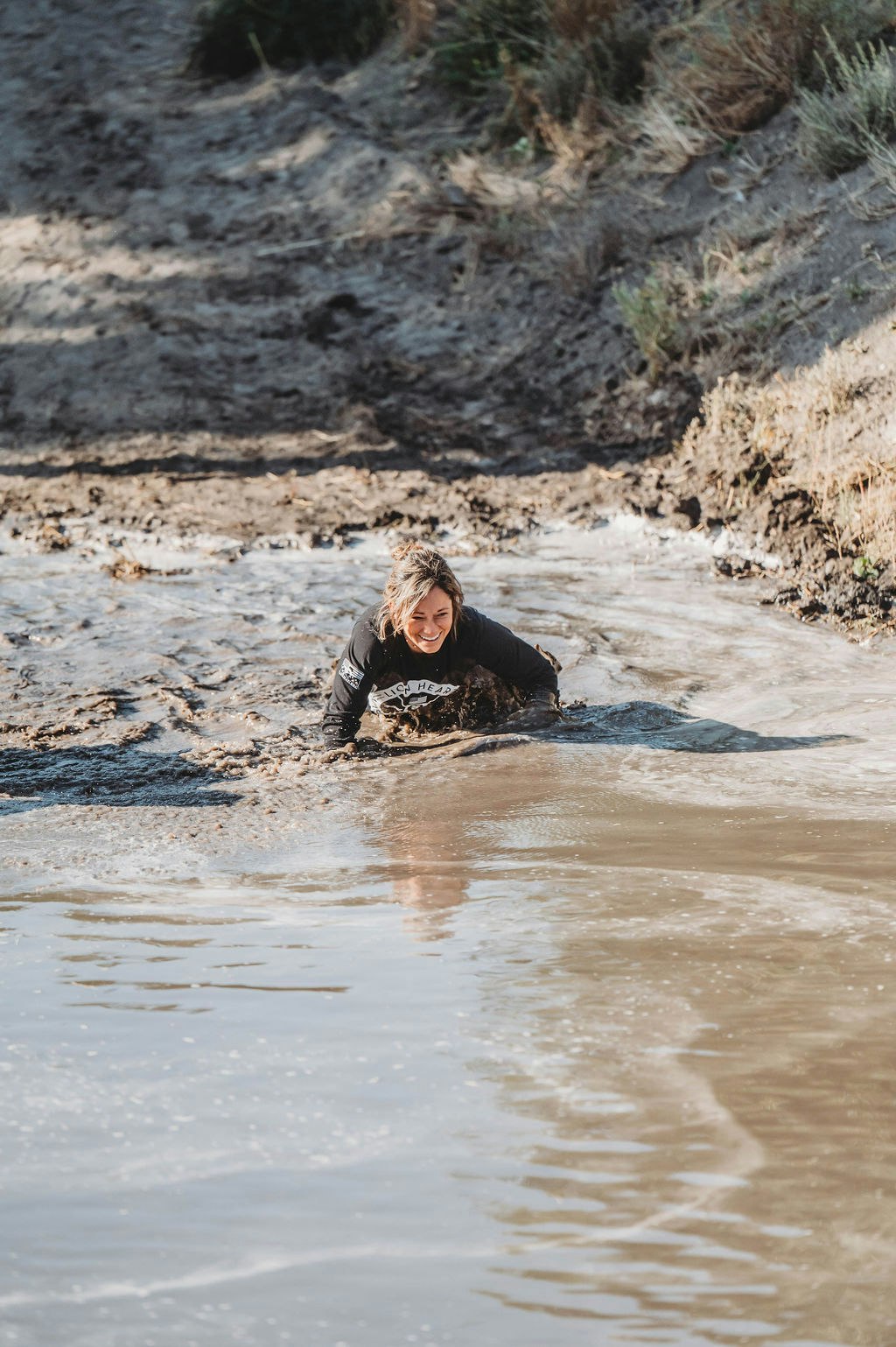 A person crawling through muddy water, smiling, during an outdoor activity.