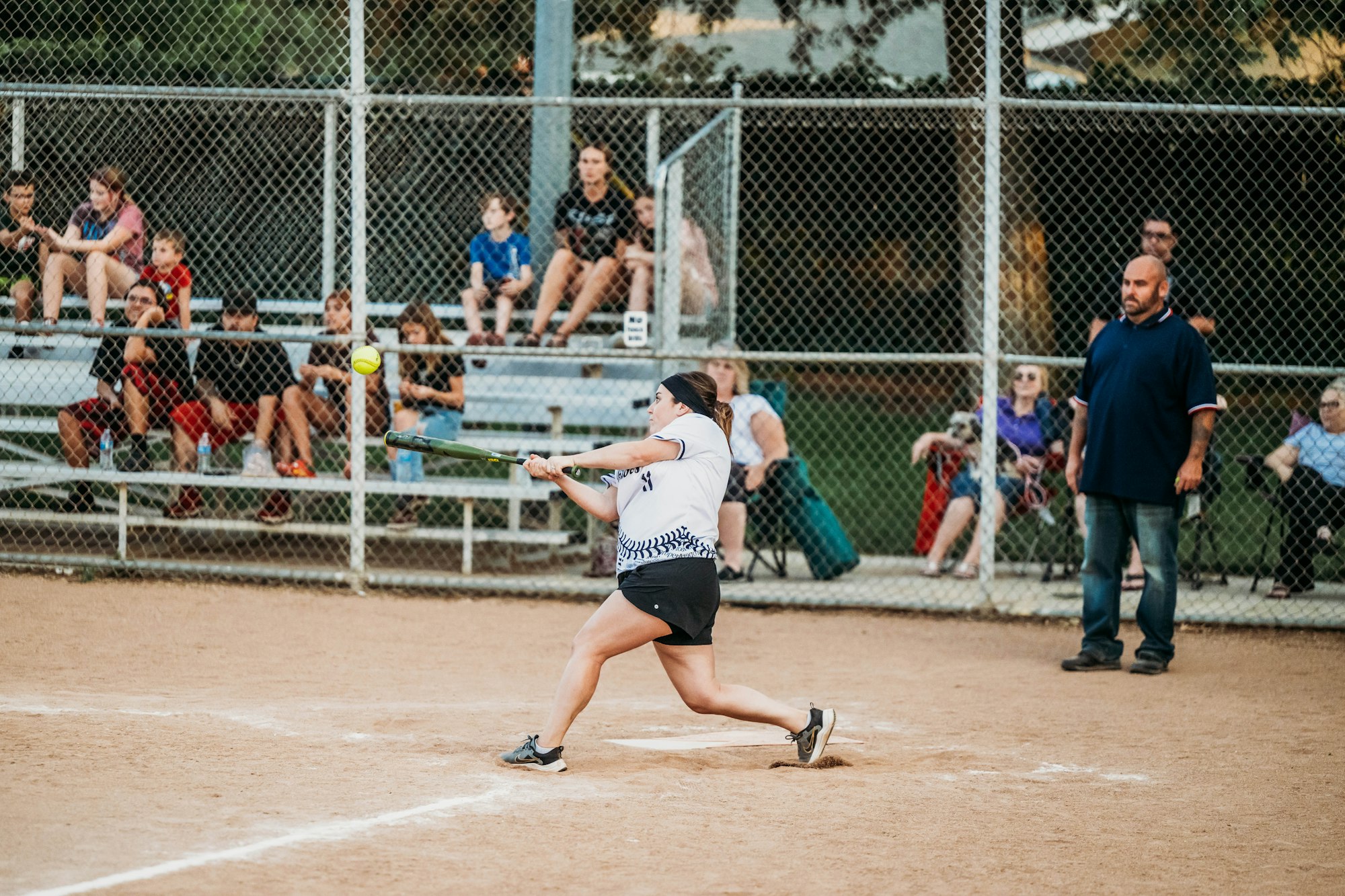 A softball player swinging at a pitch, with spectators in the background watching the game.