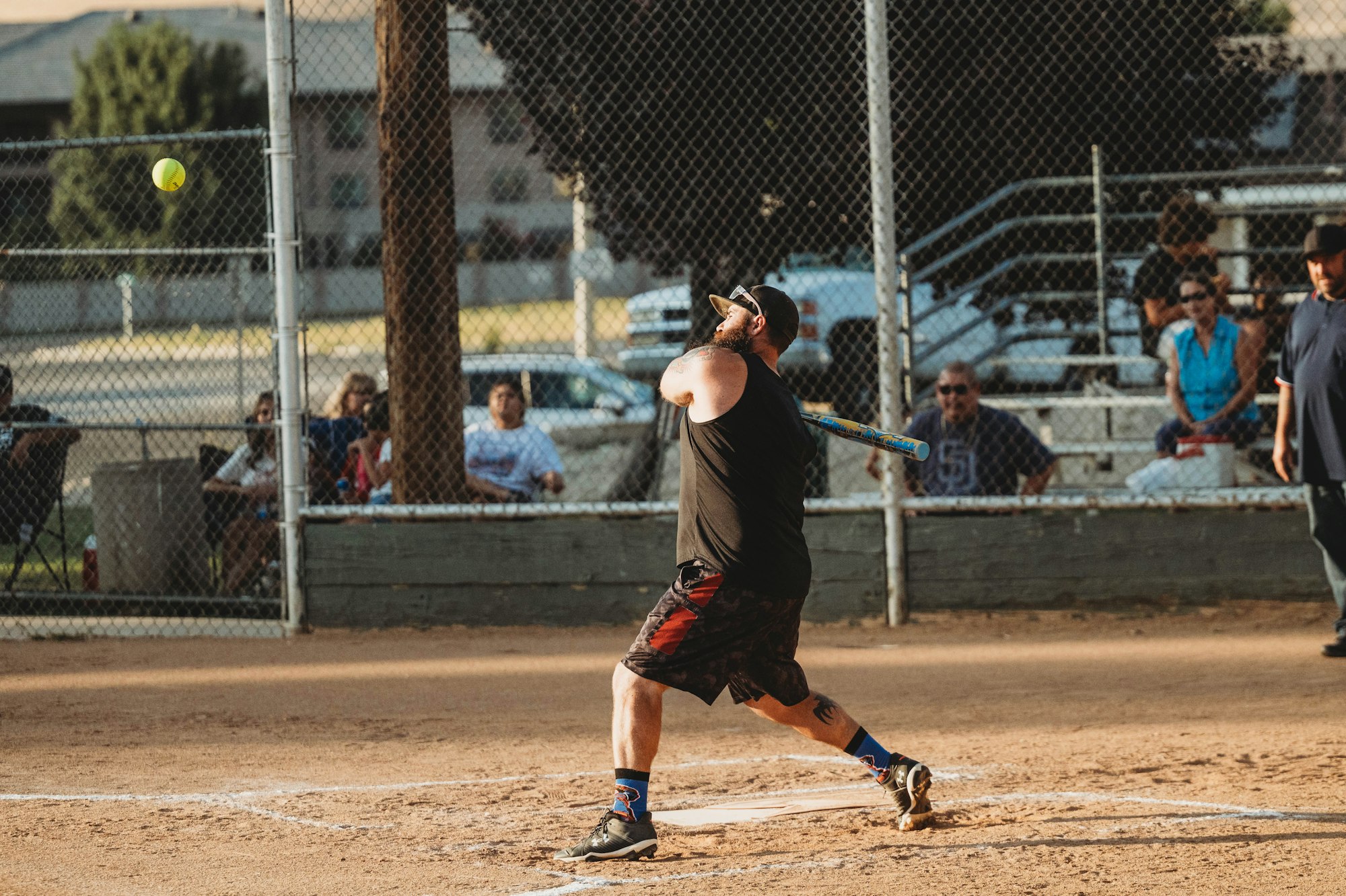 A person swinging a bat at a softball game with spectators in the background.