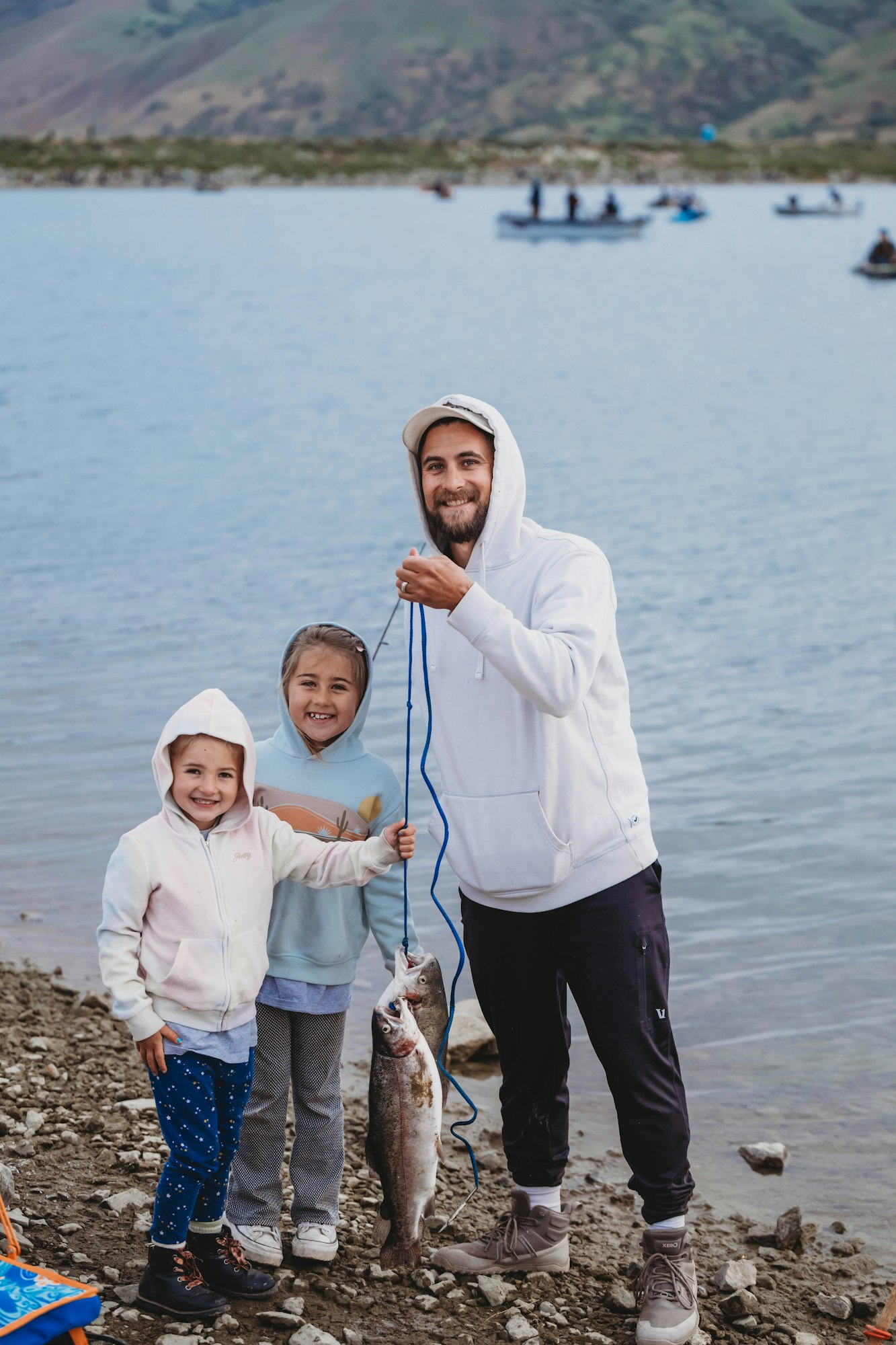 A man and two children smiling by a lake, holding a string with two caught fish.