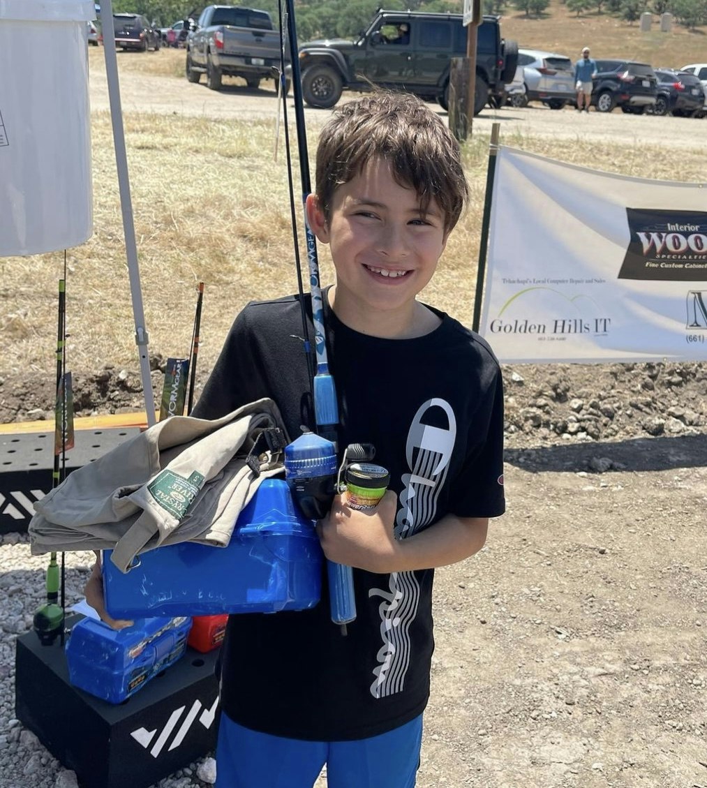 A smiling young boy holding fishing gear with cars and a banner in the background.