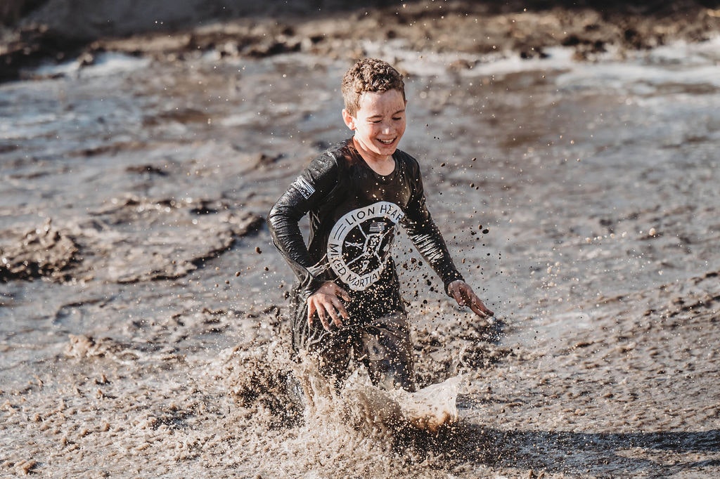 Child joyfully splashing in mud, wearing a black shirt with a graphic design.