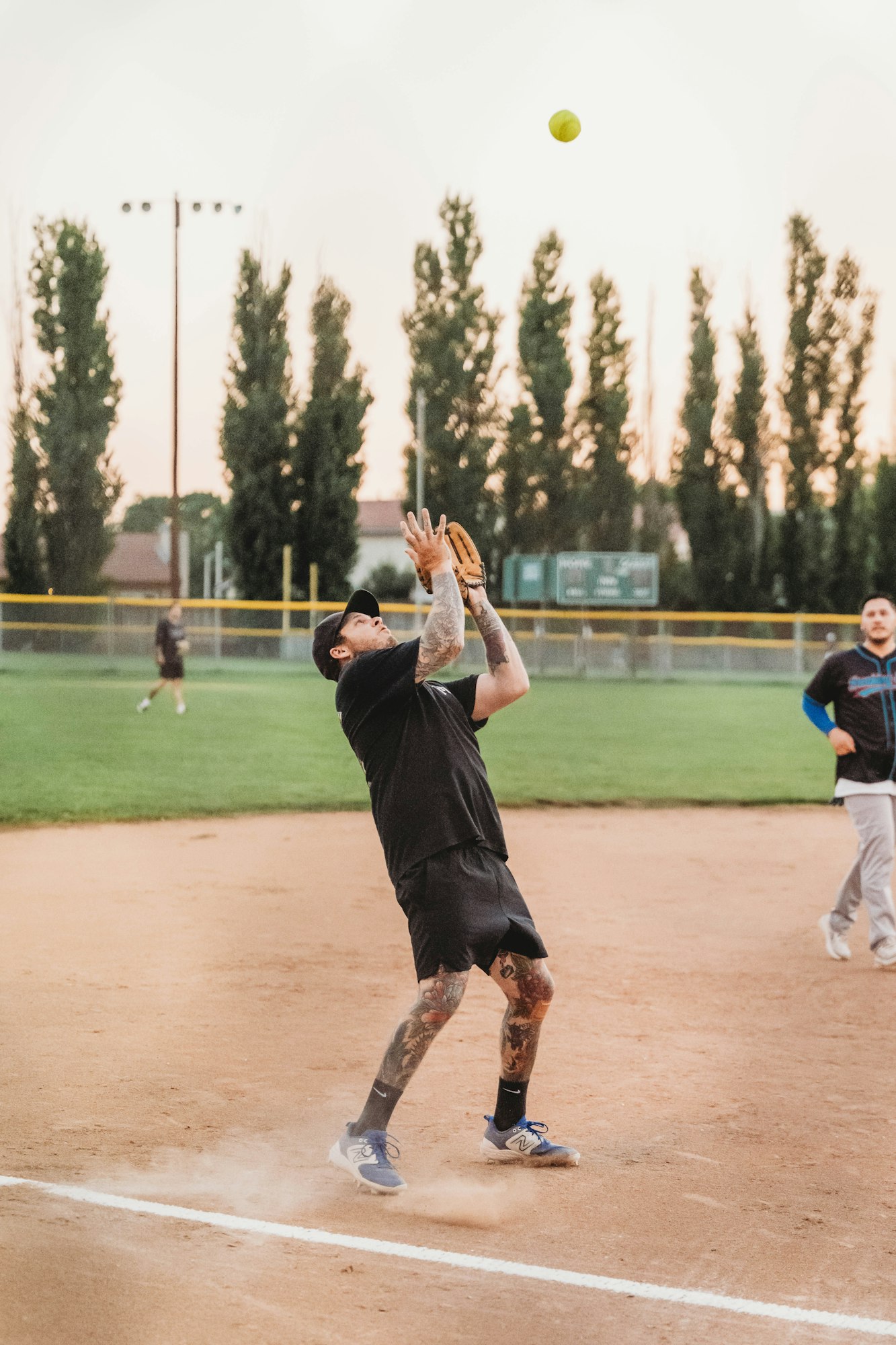 A softball game with a player catching a ball, another running, and a sunset in the background.