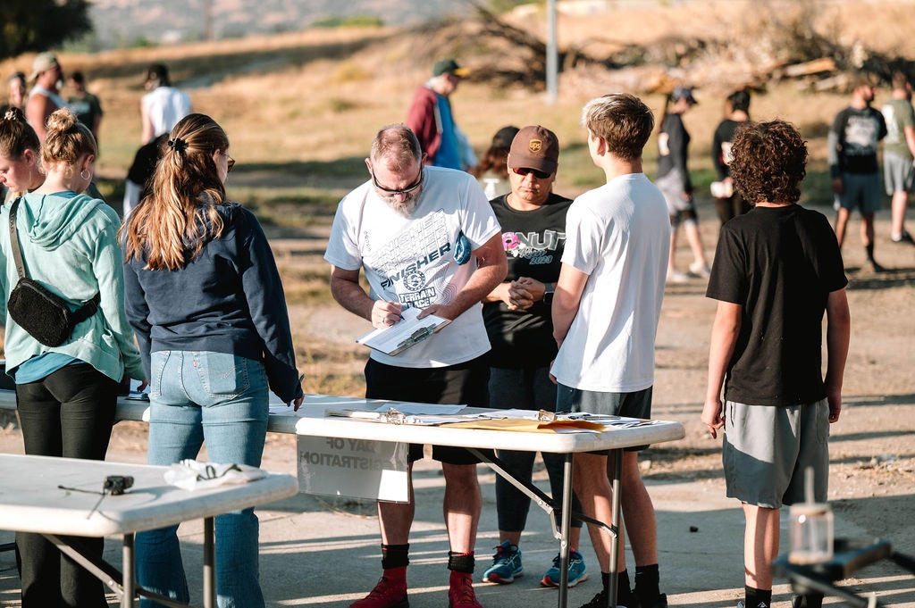 People gathered outdoors, filling out forms on tables, likely for an event or registration.